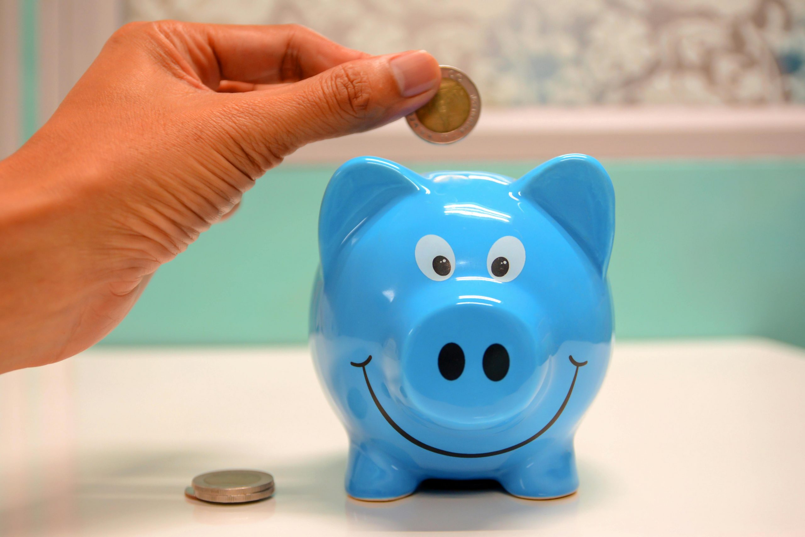 Financer votre formation : OPCO, AGEFICE, FIF PL, mode d'emploi Hand inserting a coin into a blue piggy bank for savings and money management.